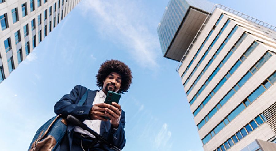 A person standing between two tall buildings, looking at a smartphone, with a clear sky and some clouds above.
