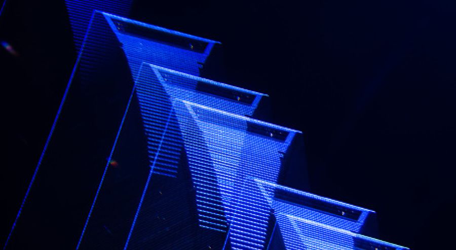 The image features abstract geometric shapes illuminated with blue light, arranged in a staggered, layered formation against a dark background to create depth and contrast.